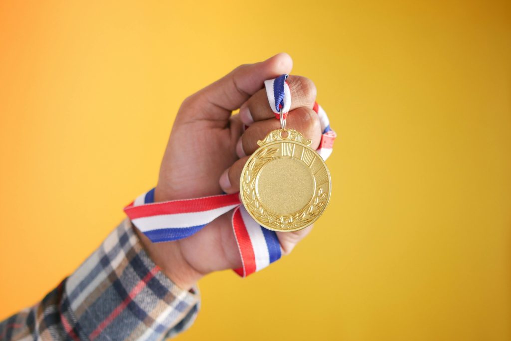 Close-up of a hand holding a gold medal with a colorful ribbon, symbolizing victory and achievement.